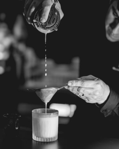 Ein Bartender gießt einen Cocktail durch ein Sieb in ein Glas.