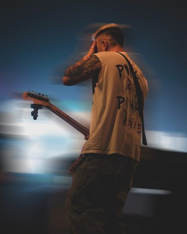 Ein Musiker mit Gitarre, der emotional auf der Bühne steht und den Kopf in die Hand legt.