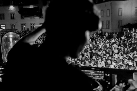 Silhouette eines DJs vor einer großen, feiernden Menschenmenge.