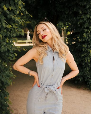 Frau mit blonden Haaren in einem blauen Kleid, posiert vor einer grünen Kulisse.