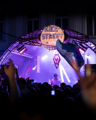 Bühne mit bunten Lichtern, Menschenfeier und Musik während eines Straßenfestes.