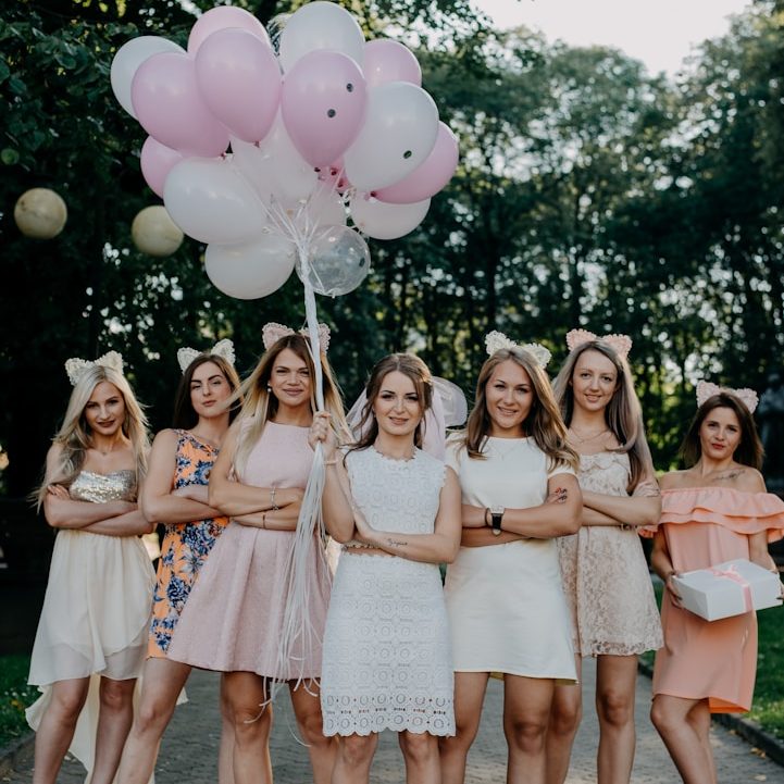 Gruppe von Frauen in festlicher Kleidung, halten Ballons und posieren im Freien.