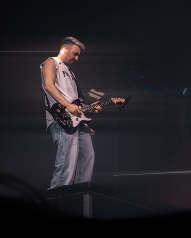 Ein Musiker mit E-Gitarre steht auf einer Bühne und spielt leidenschaftlich.